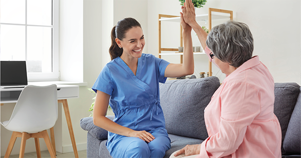 A carer and care reciever sitting on a couch giving each other a high five